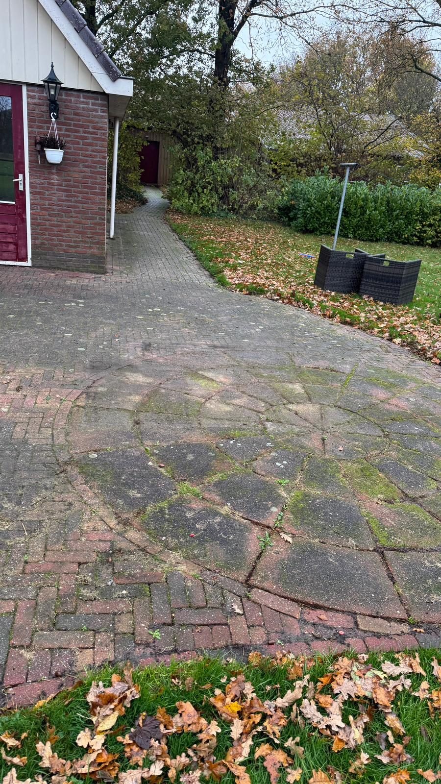 Voor: terras van klinkers met een rozet bij een woning met rode deur, grijs van mos en algen