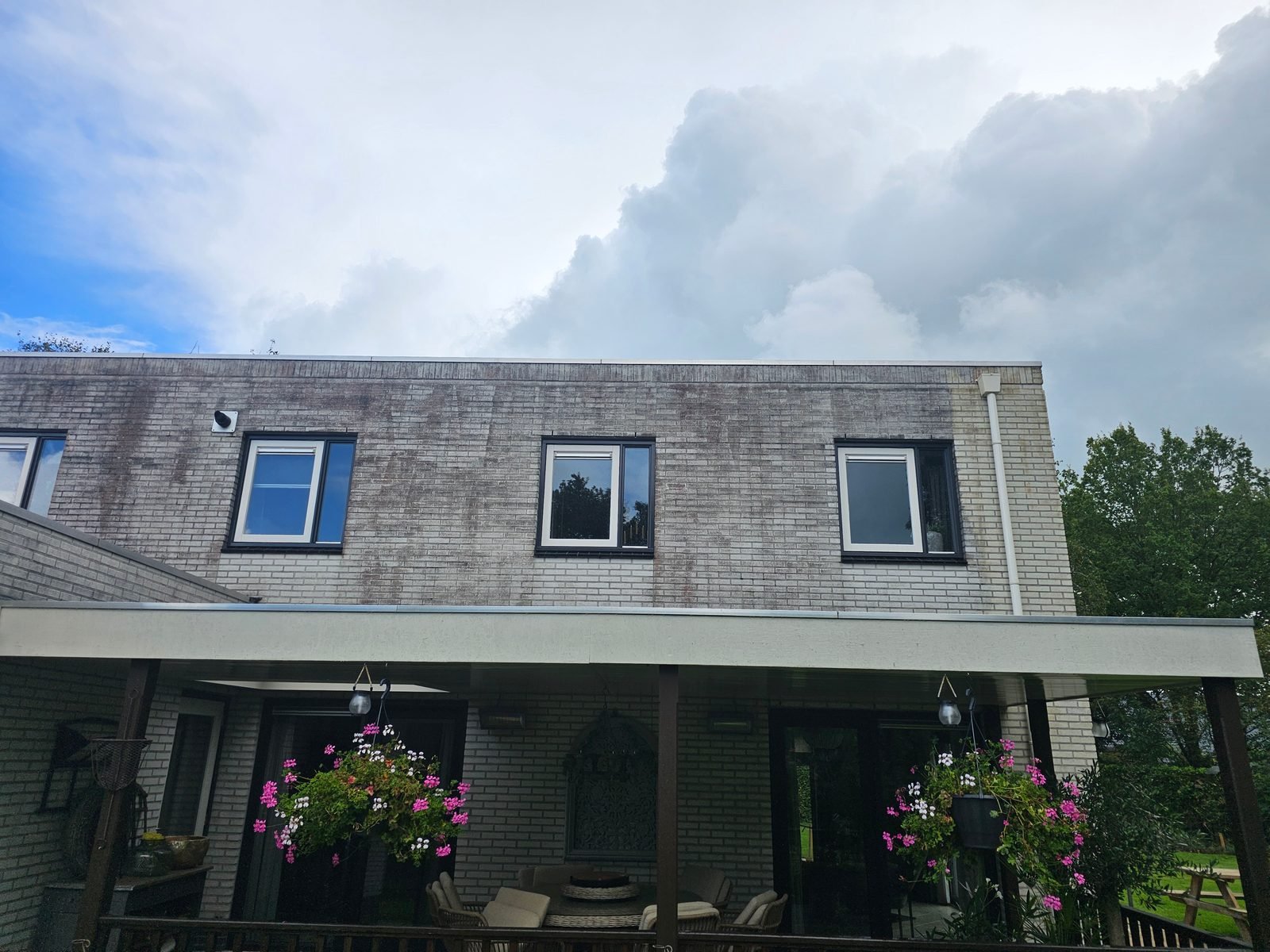 Voor: witte woning met platte overkapping, de bovenverdieping met donkere aanslag