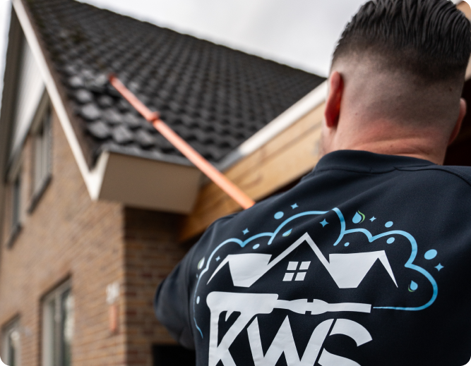 Kees van achteren op een donker pannendak, met de steel van de reiniger in zijn hand