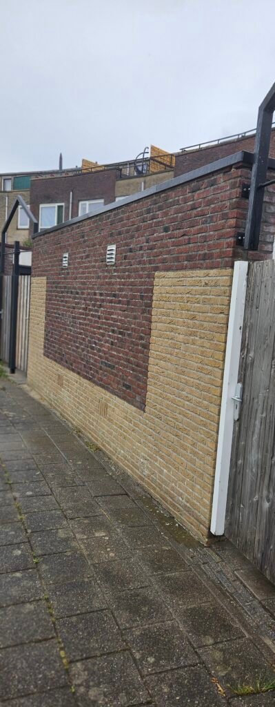 Steeg met een lage bakstenen muur, een houten schutting en klinkers.