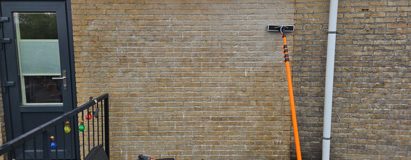 Borstel op een telescoopsteel tegen een bakstenen gevel