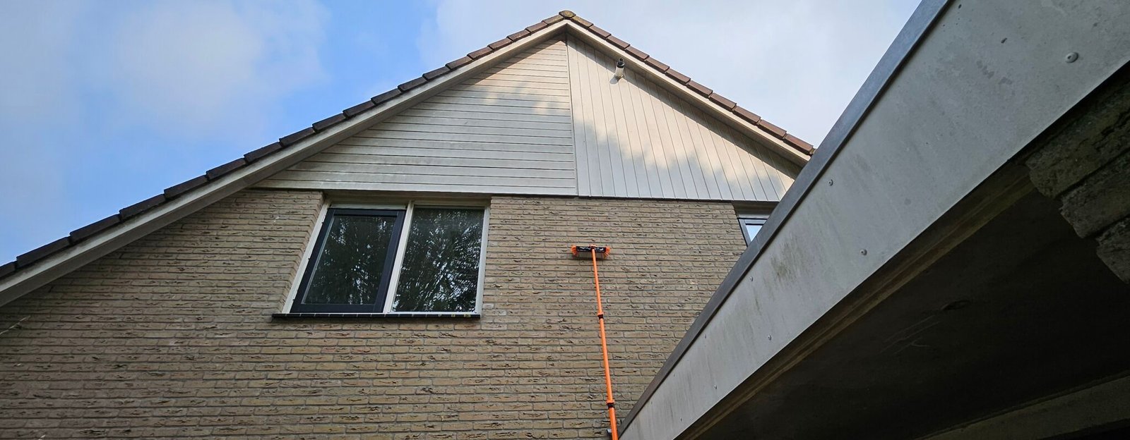 Telescoopsteel tegen de bakstenen gevel van een woning, met lichte gevelbeplating in de gevelpunt