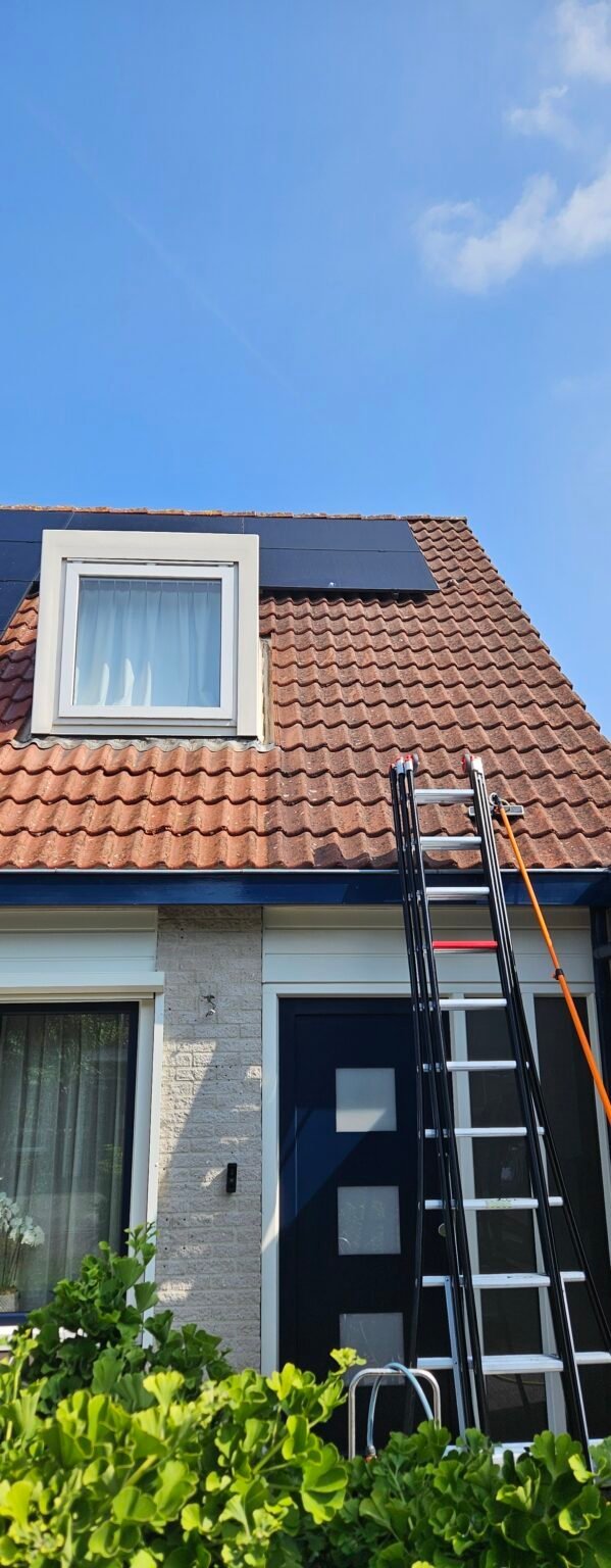 Woning met een rood pannendak en dakkapel, met een ladder tegen de dakgoot