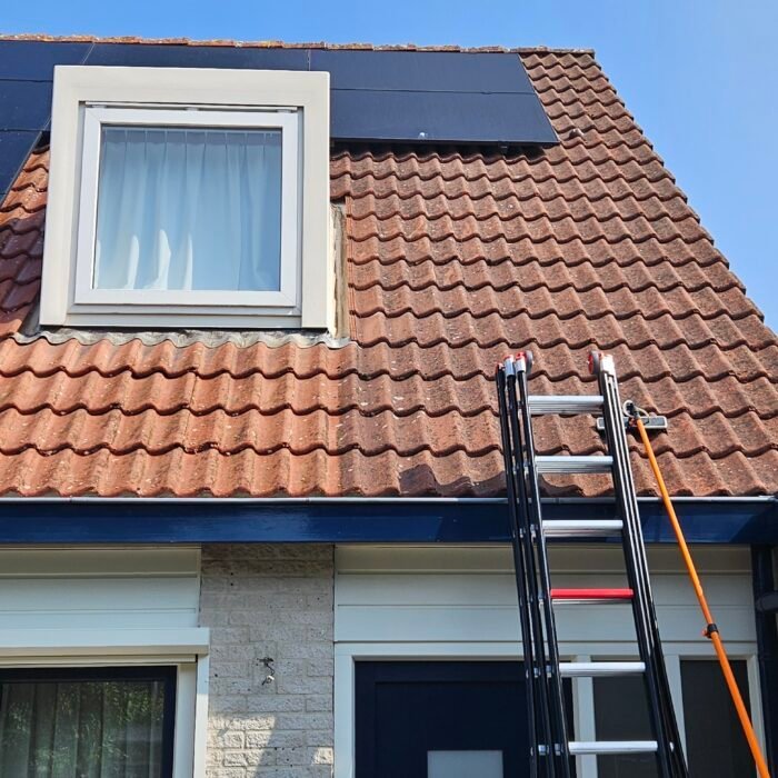 Rood pannendak met een dakkapel en zonnepanelen, met een ladder tegen de gevel