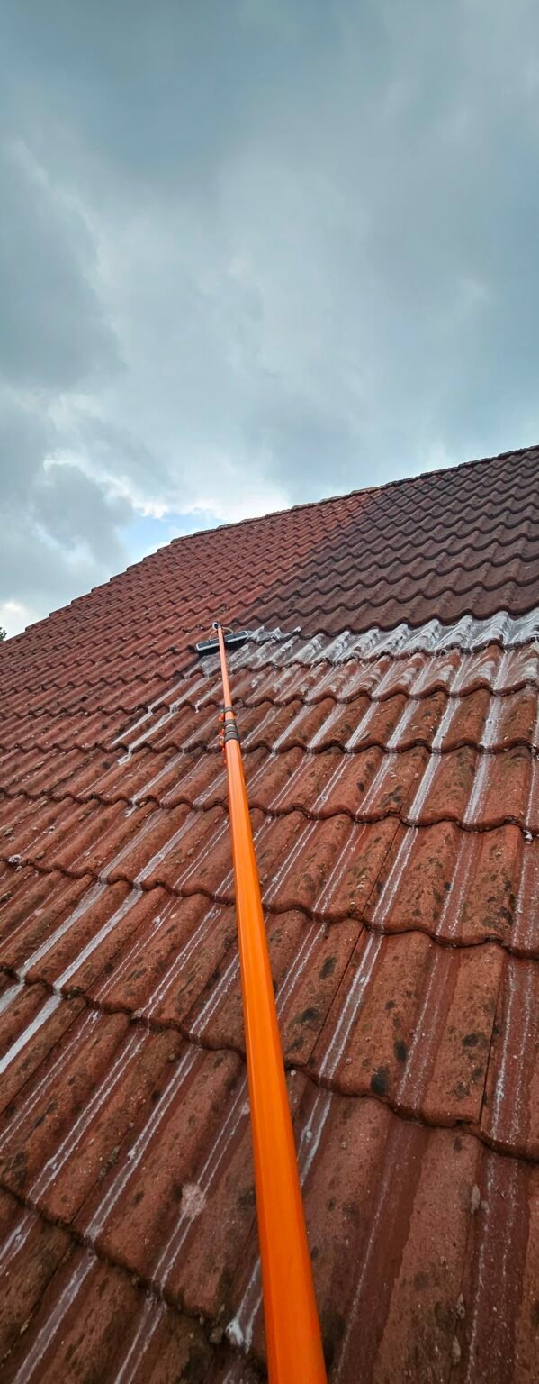 Rood pannendak tijdens het werk, met een oranje telescoopsteel op de pannen; het bovenste deel is al bewerkt, het onderste nog niet
