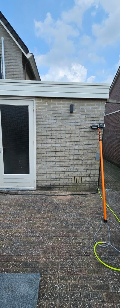Bakstenen achtergevel van een woning met een terras van klinkers, een gele slang en een steel op de grond