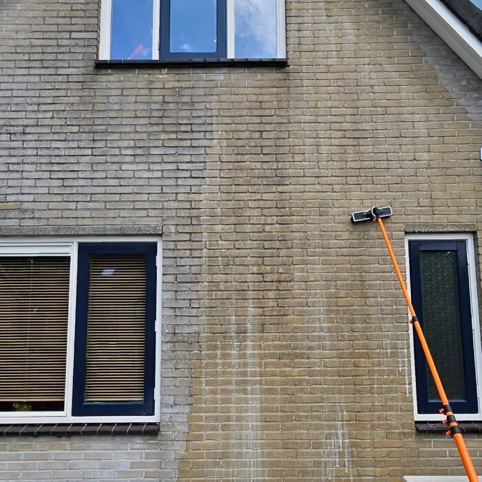 Borstel op een oranje telescoopsteel tegen een bakstenen gevel, tussen twee ramen