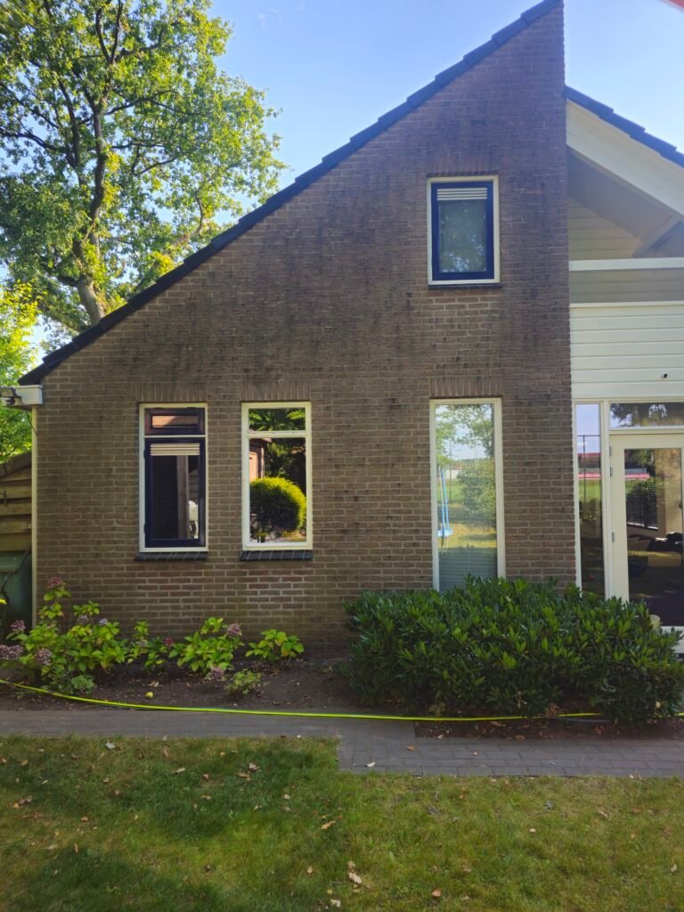Voor: bakstenen woning met puntgevel en drie ramen, donker en groen van aanslag